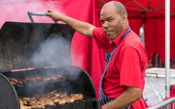 2017 food vendor standing by grill with chicken, smiling for camera.