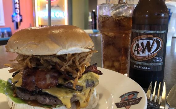 A large beef burger with bacon and cheese and a glass of Root Beer