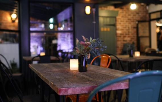 A wooden table with a candle and flowers in glass cups in a warmly lit Lost Bar and Pizzeria