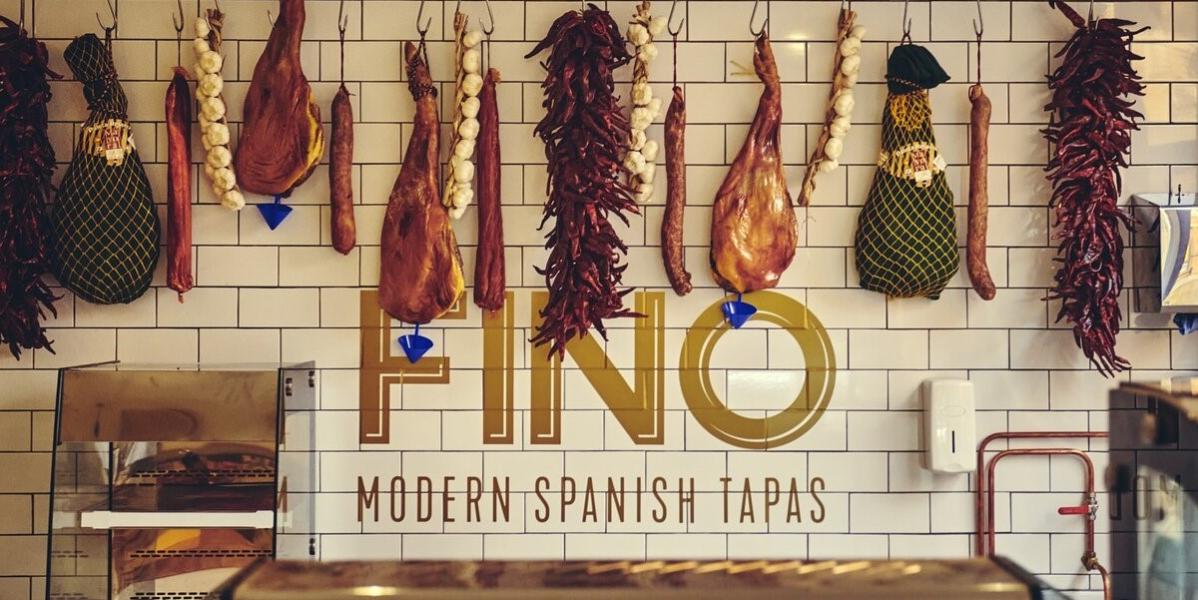 A variety of meats hung on a wall above a sign saying "Fino Modern Spanish Tapas"