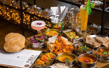 A large platter of food from Mowgli Street Food with breads for dipping, tiffin boxes of rice and meat, and tubs of curry sauces