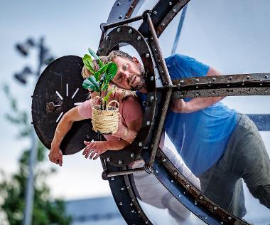 Man peeping out of Timeless installation holding a potted plant