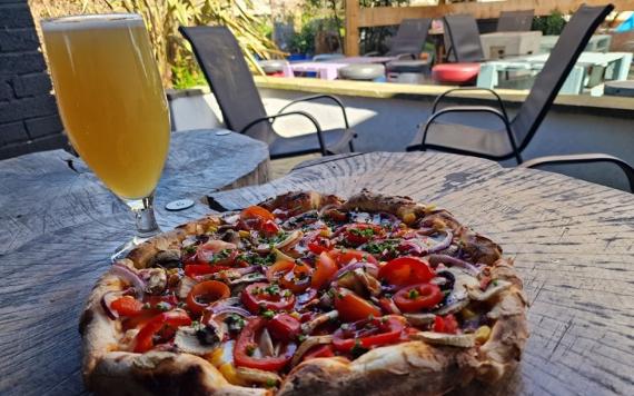 A glass of beer and a wood fired pizza on a table in the beer garden of The Moorbrook Inn