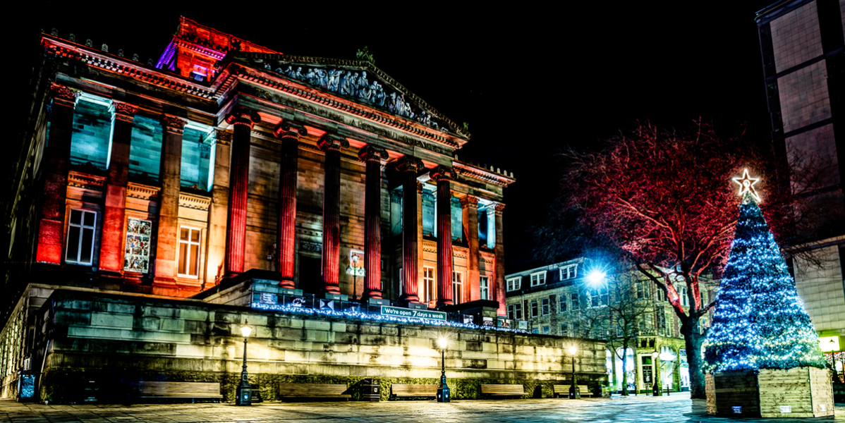 Christmas In Preston banner image A night photo of the front of The Harris building lit up with colourful lights and a Christmas tree with colourful lights
