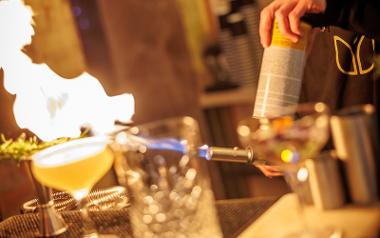 A bar man creating a drink and using a blow torch on it