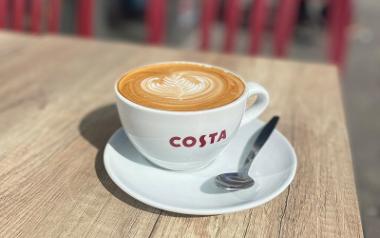 A Costa coffee mug filled with a coffee on a table