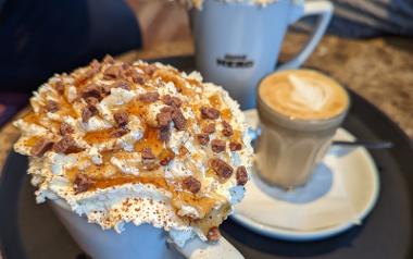 A close up of a cup of coffee with whipped cream, caramel drizzle and chocolate chips on top