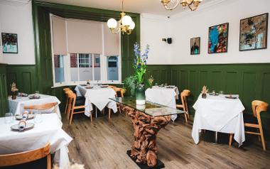 Wooden chairs and dining tables covered with white cloths inside Aven Restaurant