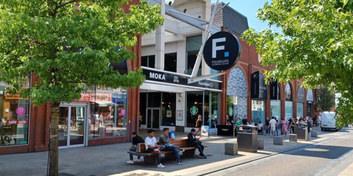 Outside the main entrance to Fishergate Shopping Centre with people sat on benches in the sun