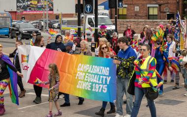 A group of people marching with the Pride Parade holding a large rainbow banner