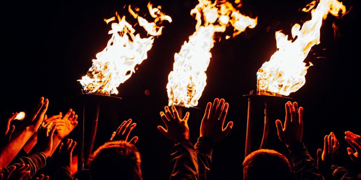 Hands raised in front of lit fire torches