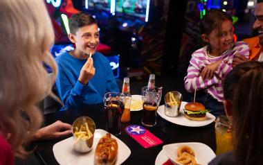 A family smiling and eating fries and burgers with cokes at Hollywood Bowl Preston