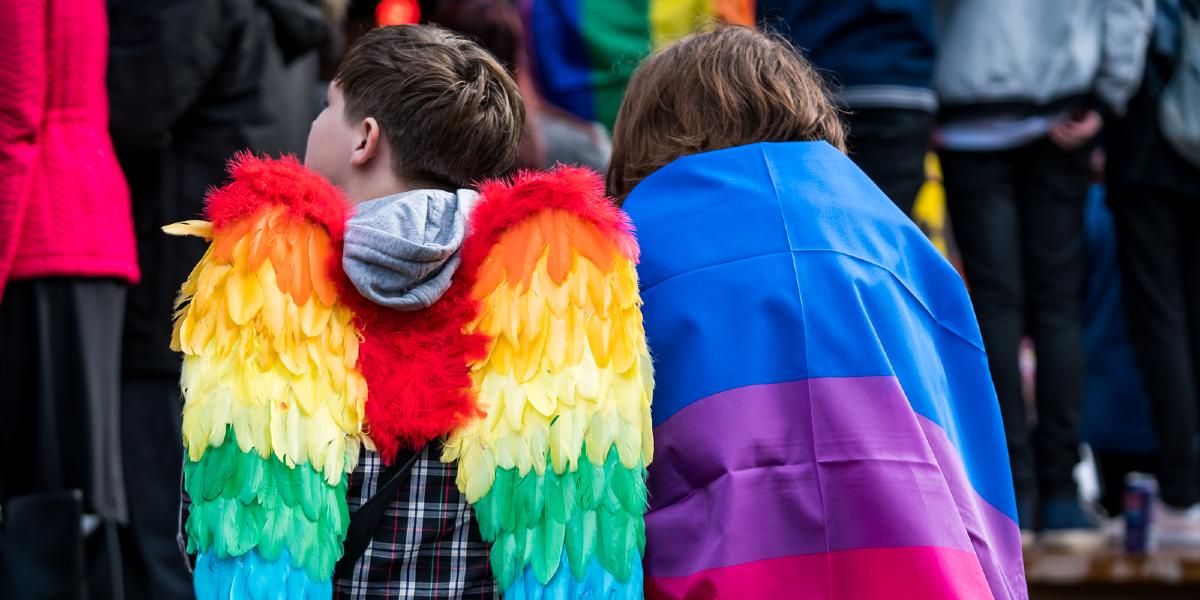 Boy with rainbow fairy wings and girl draped in a pride flag.