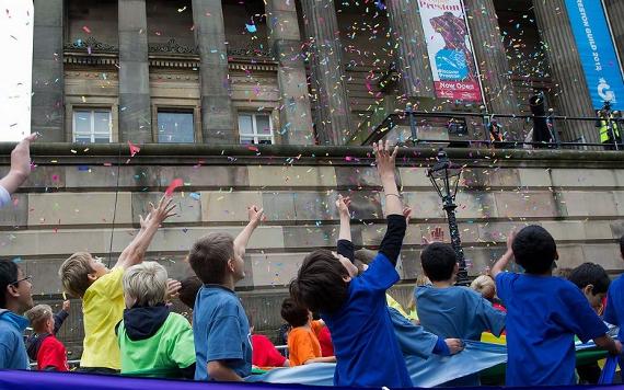 Children reaching at confetti in 2012 Guild community procession outside the Harris Museum.