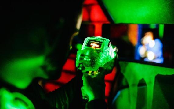 Player pointing laser tag gun at friend inside End of Days laser tag arena.