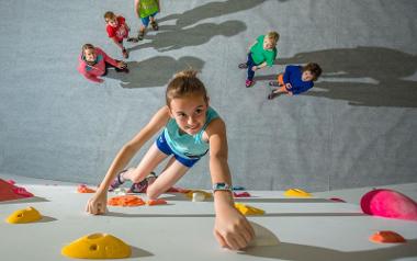 Four children watching girl climbing on Boulder UK's indoor climbing wall.