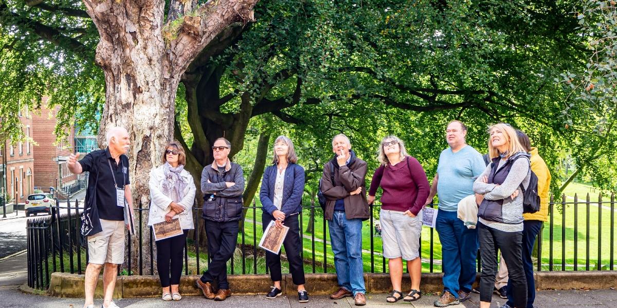 Tour guide gesturing at building on Winckley Square to group of men and women.