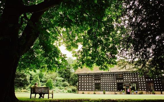 Man sitting on bench outside Samlesbury Hall on a sunny day.