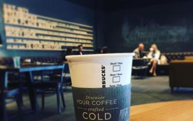 Starbucks coffee cup in foreground with people dining in background.