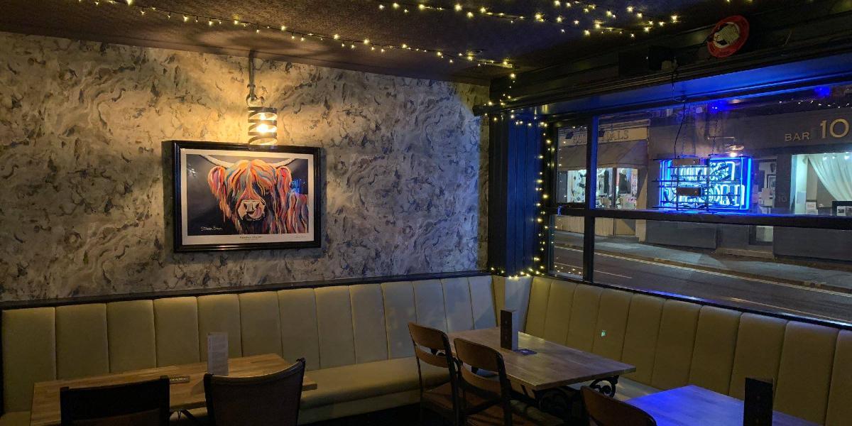 Bench seating and tables inside The Angel, with fairy lights and artwork on walls.