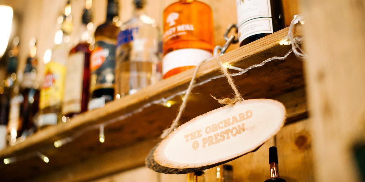 Wooden sign for The Orchard hanging by spirits behind bar.