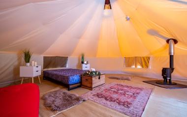 Inside a bell tent at Stanley Villa Farm with a bed and wood burning stove