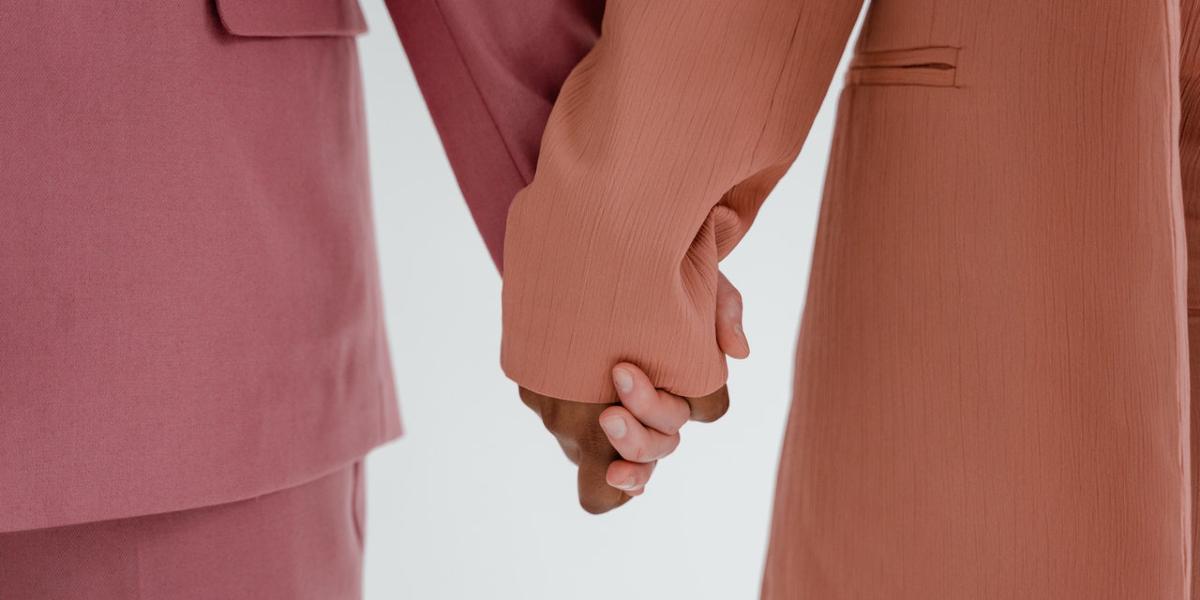 Two woman in colourful suits holding hands.