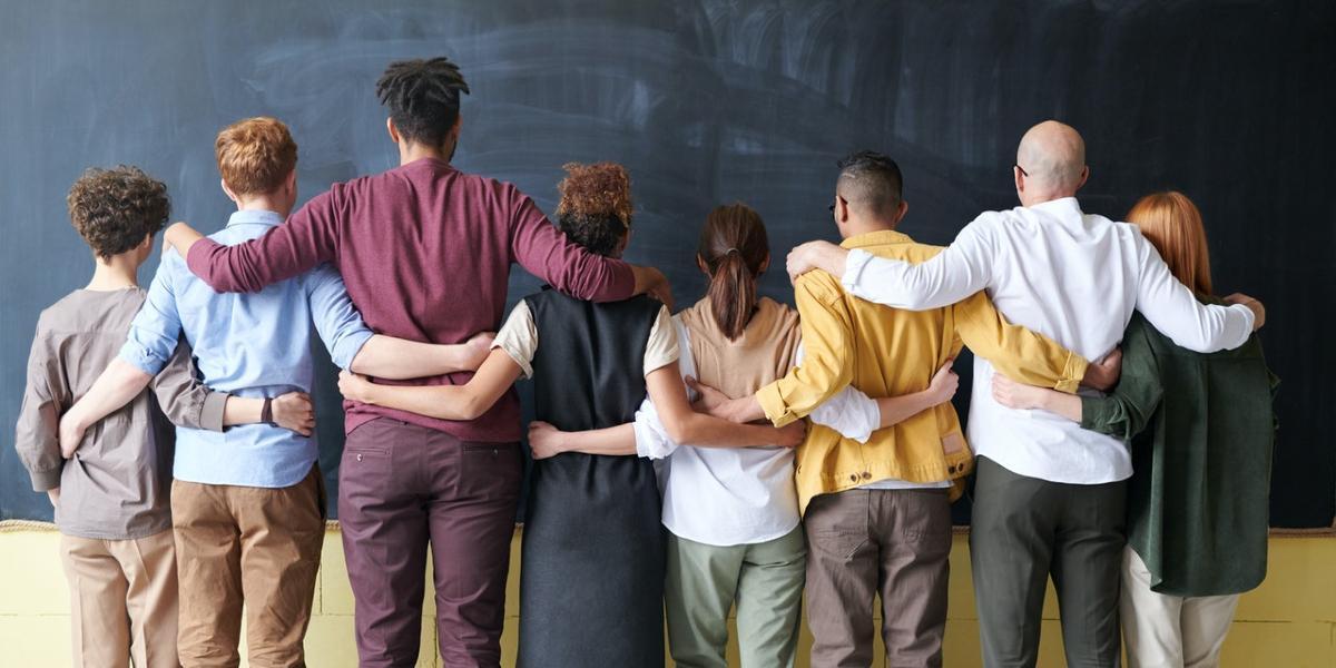 Diverse group of people with arms around each other facing away from camera.