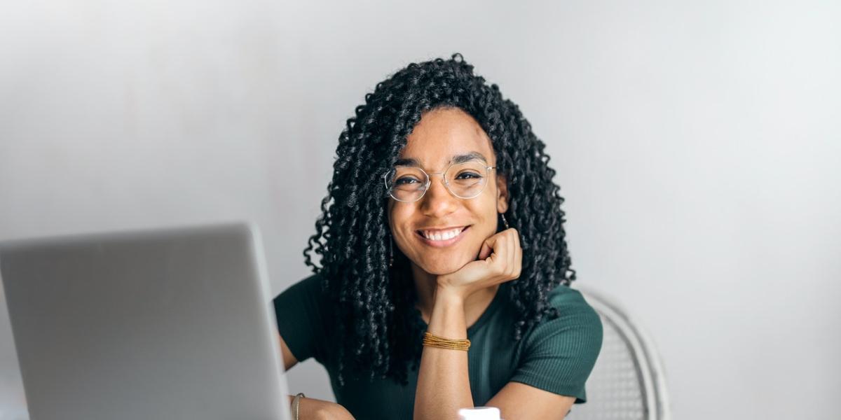 Woman sat at desk with computer smiling at camera.