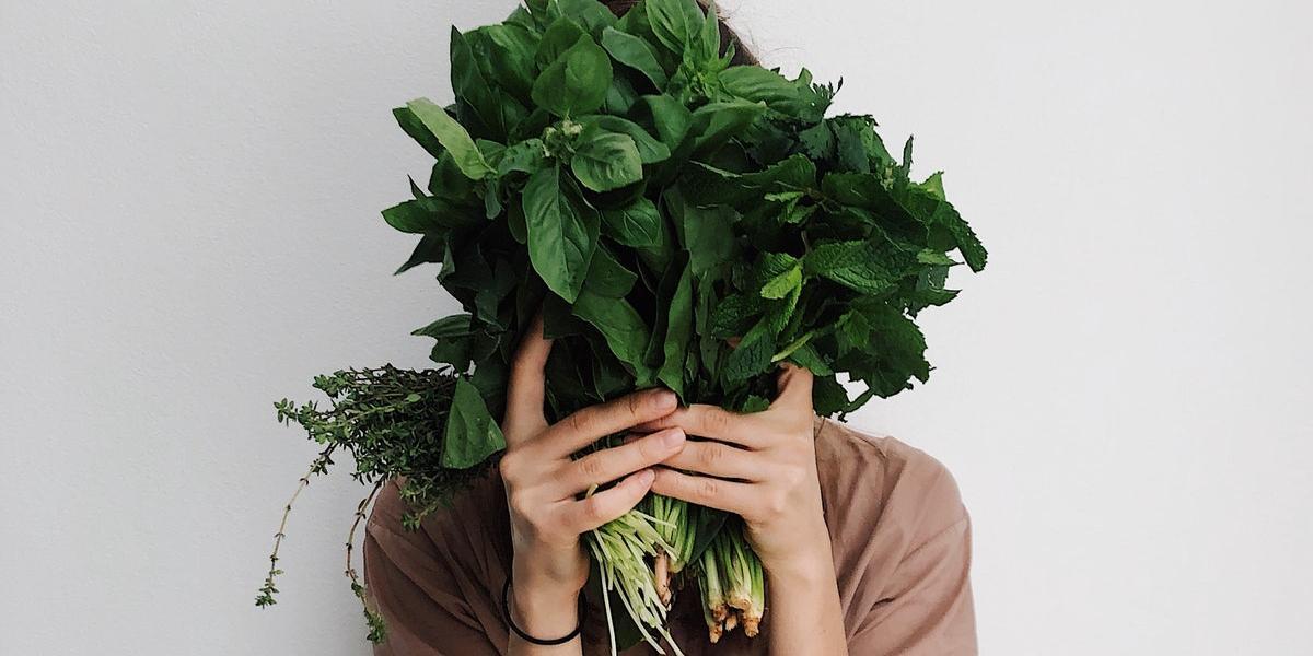 Woman hiding her face with bunch of spinach and herbs.